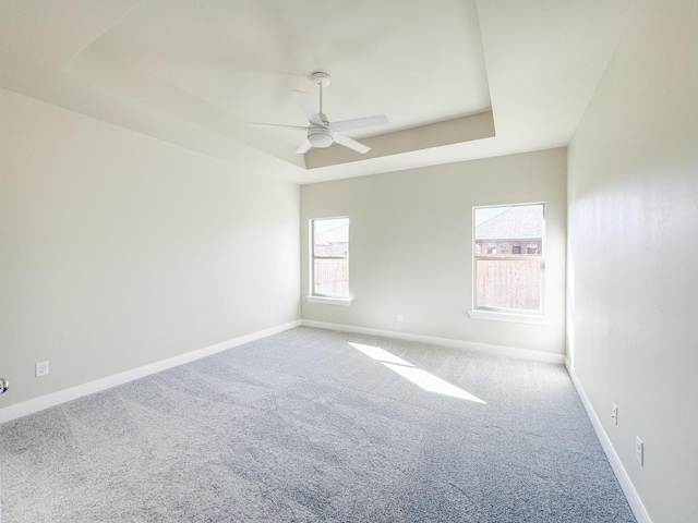 carpeted empty room with ceiling fan and a tray ceiling