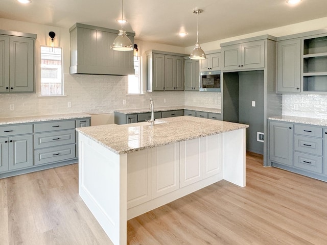 kitchen with pendant lighting, stainless steel microwave, sink, a center island with sink, and light hardwood / wood-style flooring