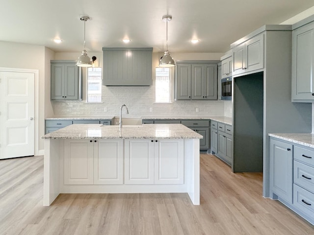 kitchen with pendant lighting, light stone countertops, and an island with sink