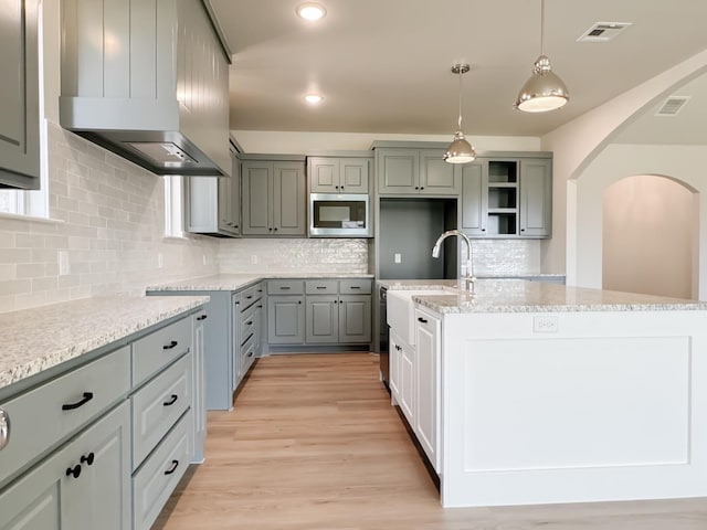 kitchen with ventilation hood, an island with sink, hanging light fixtures, and gray cabinets