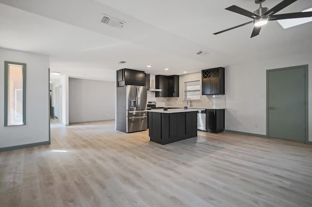 kitchen featuring wall chimney exhaust hood, appliances with stainless steel finishes, a kitchen island, light hardwood / wood-style floors, and backsplash