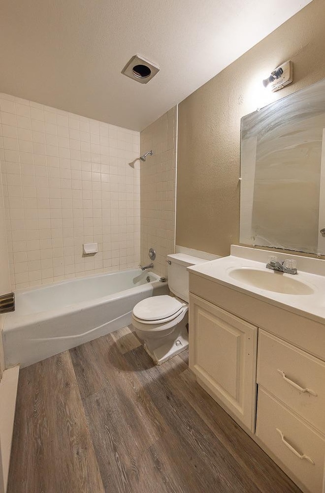 full bathroom with hardwood / wood-style flooring, vanity, tiled shower / bath combo, toilet, and a textured ceiling