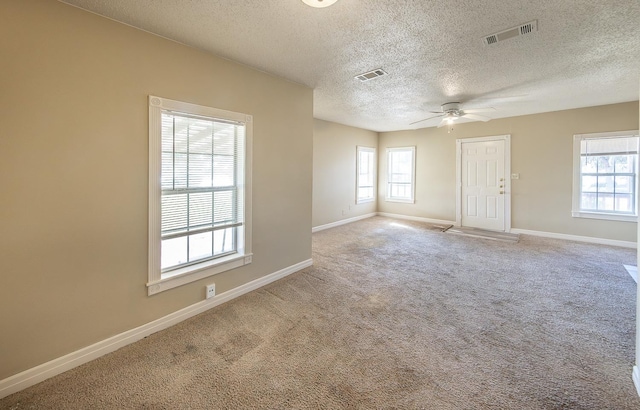 empty room featuring ceiling fan, a textured ceiling, a healthy amount of sunlight, and carpet