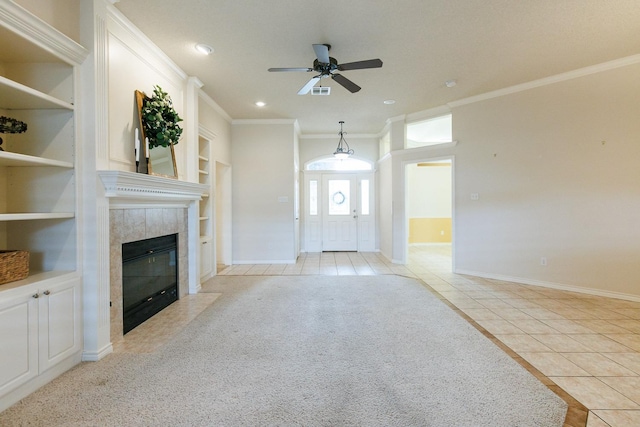 unfurnished living room with crown molding, built in features, a tile fireplace, ceiling fan, and light tile patterned flooring