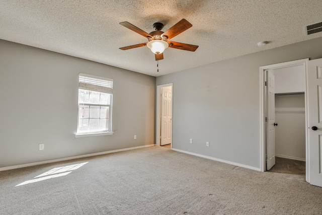 unfurnished bedroom featuring ceiling fan, a spacious closet, light carpet, and a textured ceiling