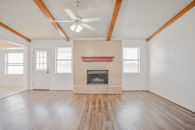 unfurnished living room with beamed ceiling, a healthy amount of sunlight, a textured ceiling, and light hardwood / wood-style floors