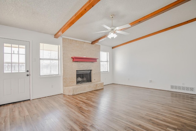 unfurnished living room featuring beam ceiling, a textured ceiling, light wood-type flooring, ceiling fan, and a fireplace