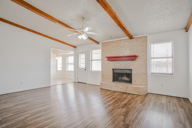 unfurnished living room featuring lofted ceiling with beams, a brick fireplace, a textured ceiling, light wood-type flooring, and ceiling fan