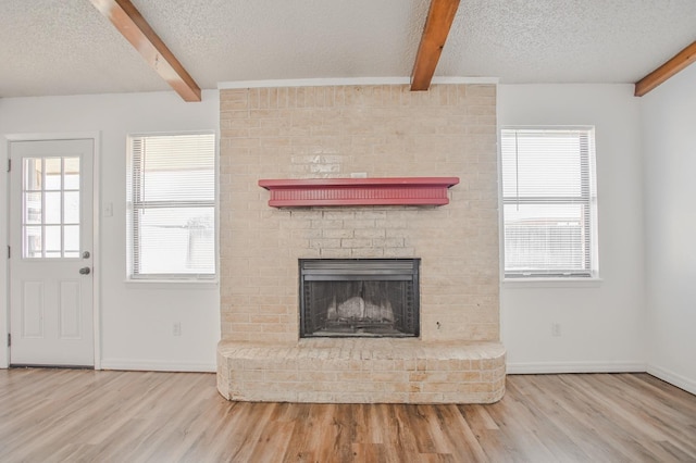 unfurnished living room with beam ceiling, light hardwood / wood-style floors, a brick fireplace, and a textured ceiling