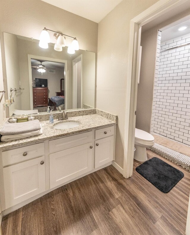 bathroom featuring wood-type flooring, vanity, tiled shower, ceiling fan, and toilet