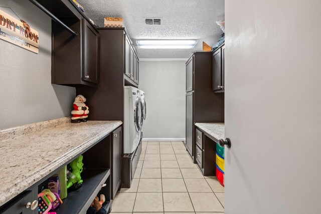 kitchen with light tile patterned flooring, dark brown cabinetry, a textured ceiling, light stone countertops, and washer and clothes dryer