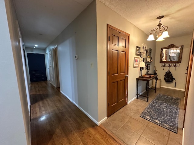 corridor featuring a notable chandelier, a textured ceiling, and light hardwood / wood-style flooring