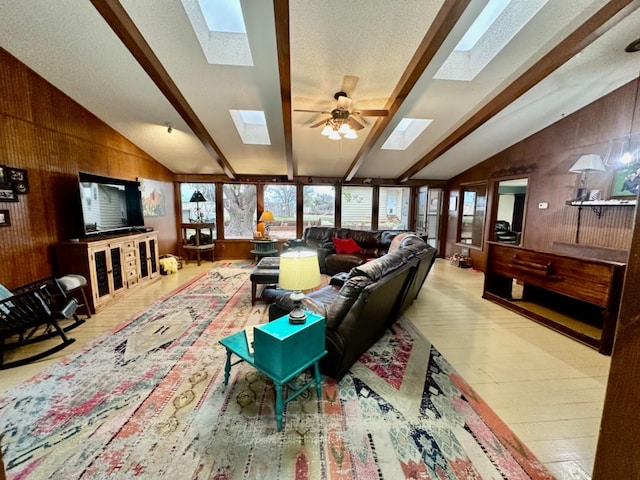 living room with ceiling fan, vaulted ceiling with skylight, light hardwood / wood-style flooring, and wood walls