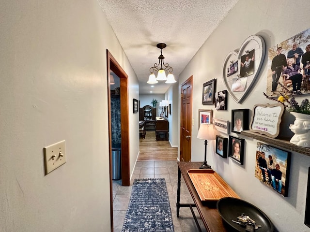 corridor with light tile patterned flooring, an inviting chandelier, and a textured ceiling