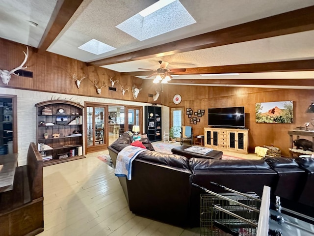 living room with a skylight, wooden walls, hardwood / wood-style flooring, ceiling fan, and beam ceiling