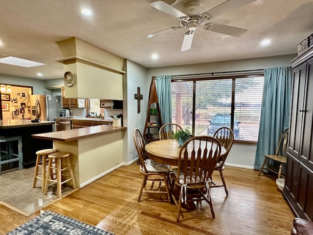 dining space with ceiling fan, light hardwood / wood-style floors, and a skylight