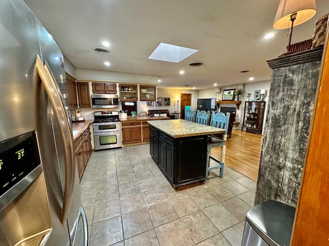 kitchen featuring a kitchen island, a skylight, a breakfast bar area, stainless steel appliances, and light stone countertops