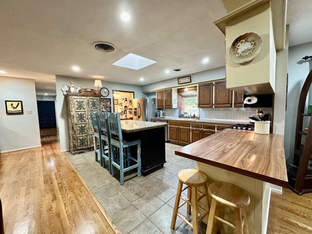 kitchen with a kitchen island, appliances with stainless steel finishes, a skylight, a breakfast bar area, and wooden counters