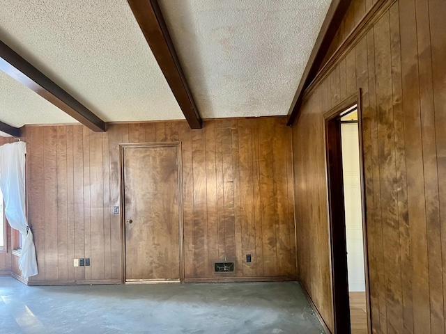 empty room featuring beamed ceiling, wooden walls, and a textured ceiling