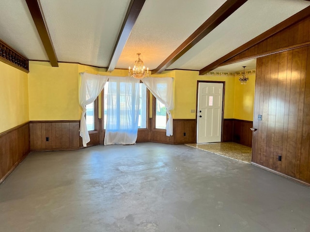 spare room with an inviting chandelier, concrete flooring, a textured ceiling, beamed ceiling, and wood walls