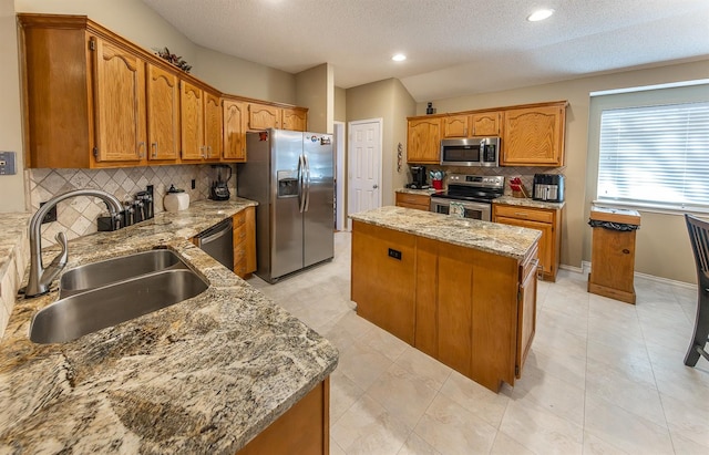 kitchen with sink, appliances with stainless steel finishes, a center island, light stone counters, and tasteful backsplash