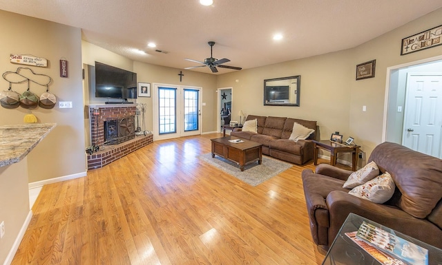 living room with ceiling fan, light hardwood / wood-style floors, a brick fireplace, and a textured ceiling