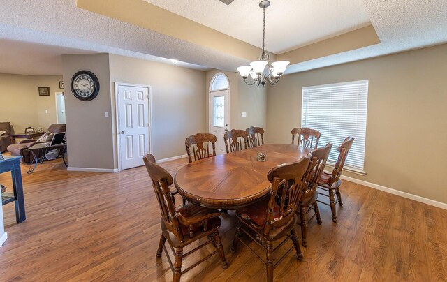 dining room featuring an inviting chandelier, hardwood / wood-style floors, a tray ceiling, and a textured ceiling