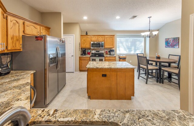 kitchen featuring appliances with stainless steel finishes, an inviting chandelier, hanging light fixtures, a center island, and a textured ceiling