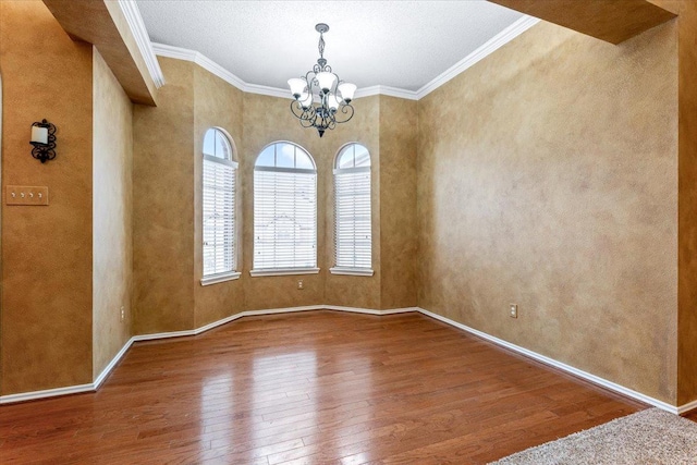 spare room with wood-type flooring, ornamental molding, and an inviting chandelier