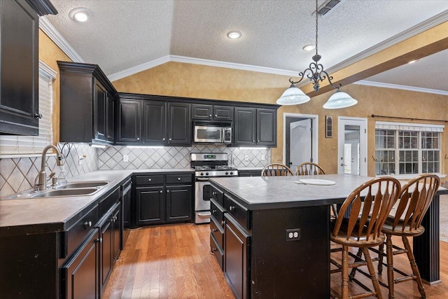 kitchen with lofted ceiling, sink, decorative light fixtures, a kitchen island, and stainless steel appliances