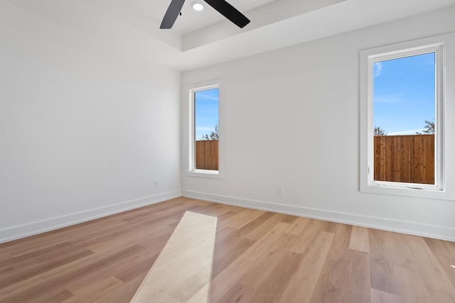 empty room featuring ceiling fan, a raised ceiling, and light wood-type flooring