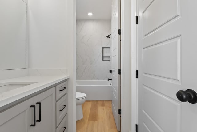 full bathroom featuring vanity, hardwood / wood-style flooring, tiled shower / bath combo, and toilet