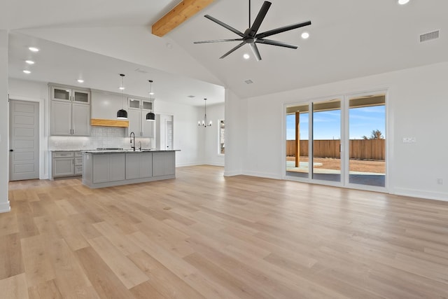 unfurnished living room with ceiling fan with notable chandelier, high vaulted ceiling, beamed ceiling, sink, and light hardwood / wood-style flooring