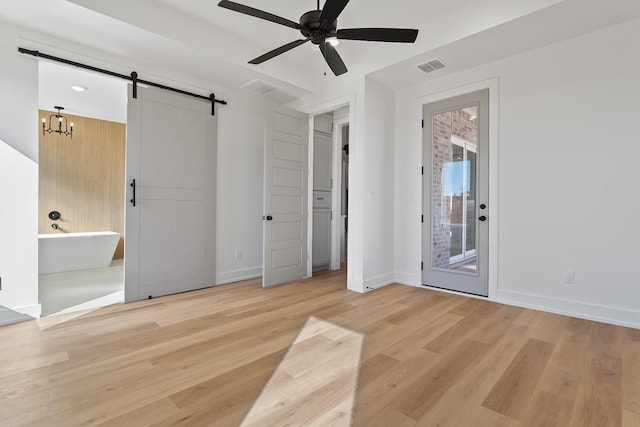 unfurnished bedroom featuring ceiling fan, a barn door, access to exterior, and light wood-type flooring