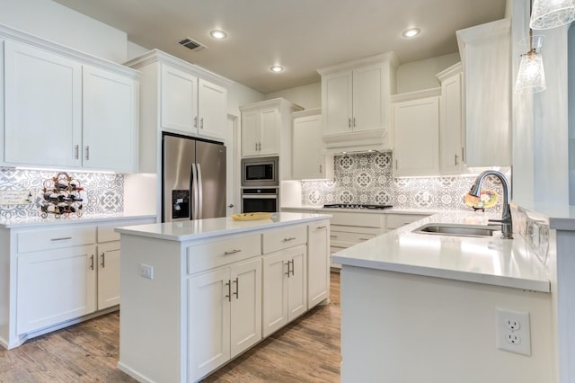 kitchen featuring appliances with stainless steel finishes, white cabinetry, sink, hanging light fixtures, and a center island