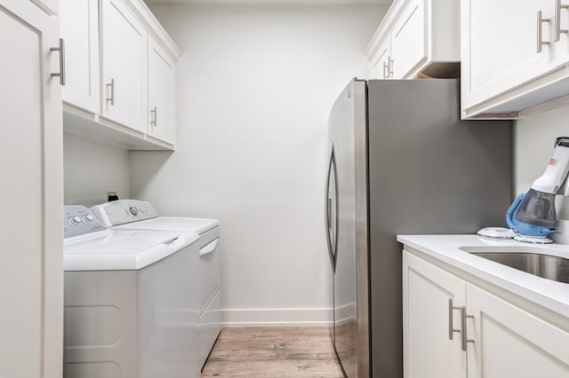 laundry area with cabinets, sink, washer and dryer, and light wood-type flooring