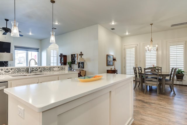 kitchen with a kitchen island, decorative light fixtures, sink, white cabinets, and light wood-type flooring