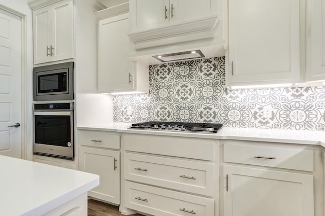 kitchen with backsplash, premium range hood, white cabinets, and appliances with stainless steel finishes