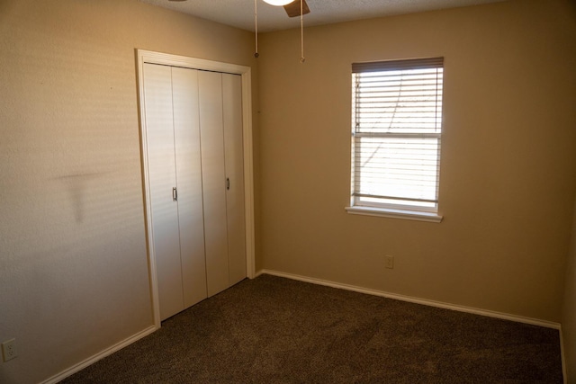 unfurnished bedroom featuring dark colored carpet, ceiling fan, and a closet