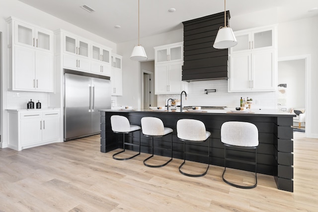 kitchen featuring tasteful backsplash, visible vents, light wood-style flooring, a breakfast bar, and stainless steel built in refrigerator