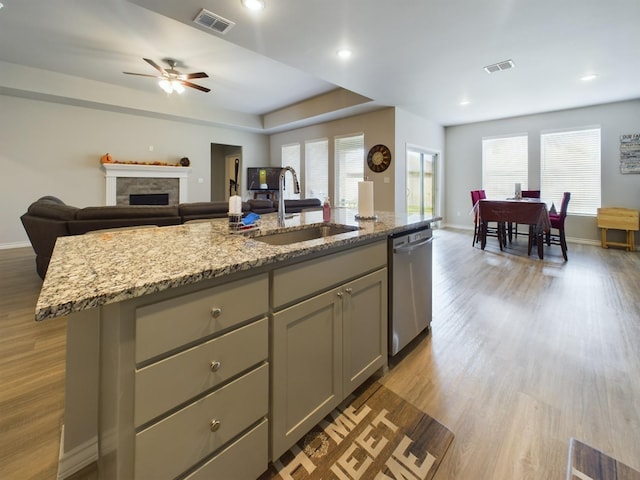 kitchen with dishwasher, sink, gray cabinetry, hardwood / wood-style flooring, and a kitchen island with sink