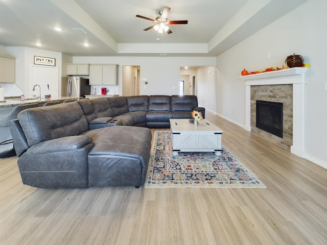 living room featuring sink, a raised ceiling, ceiling fan, and light wood-type flooring