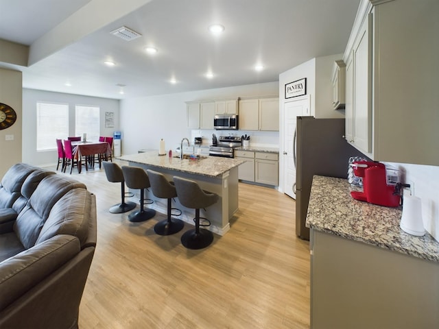 kitchen featuring appliances with stainless steel finishes, sink, light stone countertops, and an island with sink