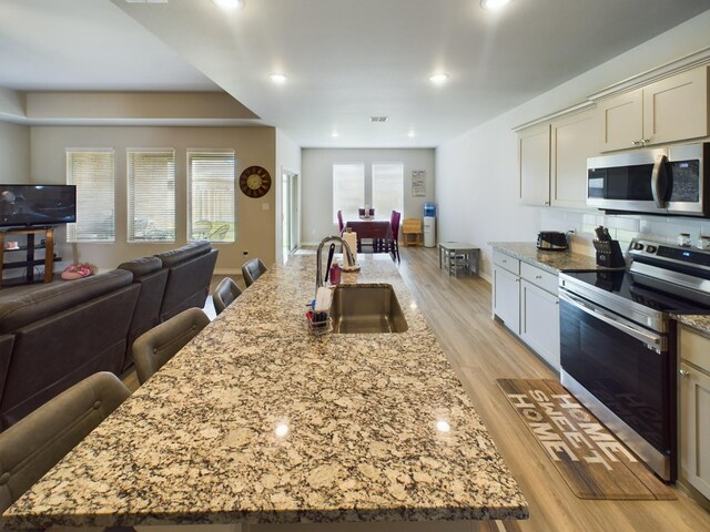 kitchen featuring sink, appliances with stainless steel finishes, a kitchen breakfast bar, light stone counters, and an island with sink