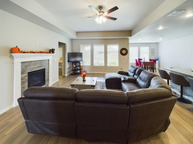 living room featuring ceiling fan, a stone fireplace, and light wood-type flooring