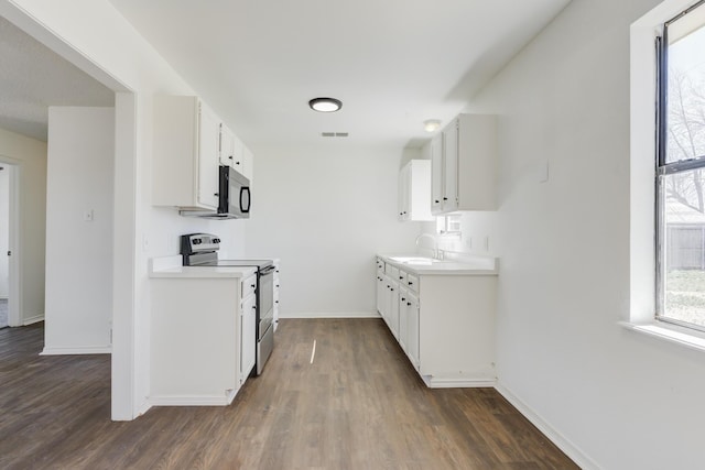 kitchen featuring stainless steel electric stove, light countertops, white cabinets, a sink, and black microwave