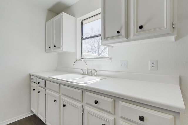 kitchen featuring baseboards, white cabinets, dark wood-style flooring, light countertops, and a sink