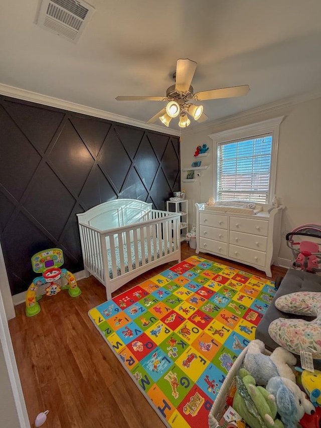 bedroom featuring crown molding, ceiling fan, hardwood / wood-style flooring, and a crib