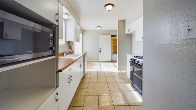 kitchen with white cabinetry, sink, gas range, and light tile patterned floors