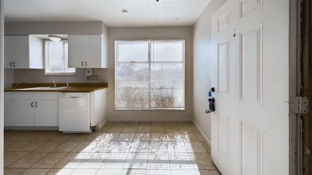 kitchen featuring dishwasher, sink, white cabinets, light tile patterned floors, and a textured ceiling